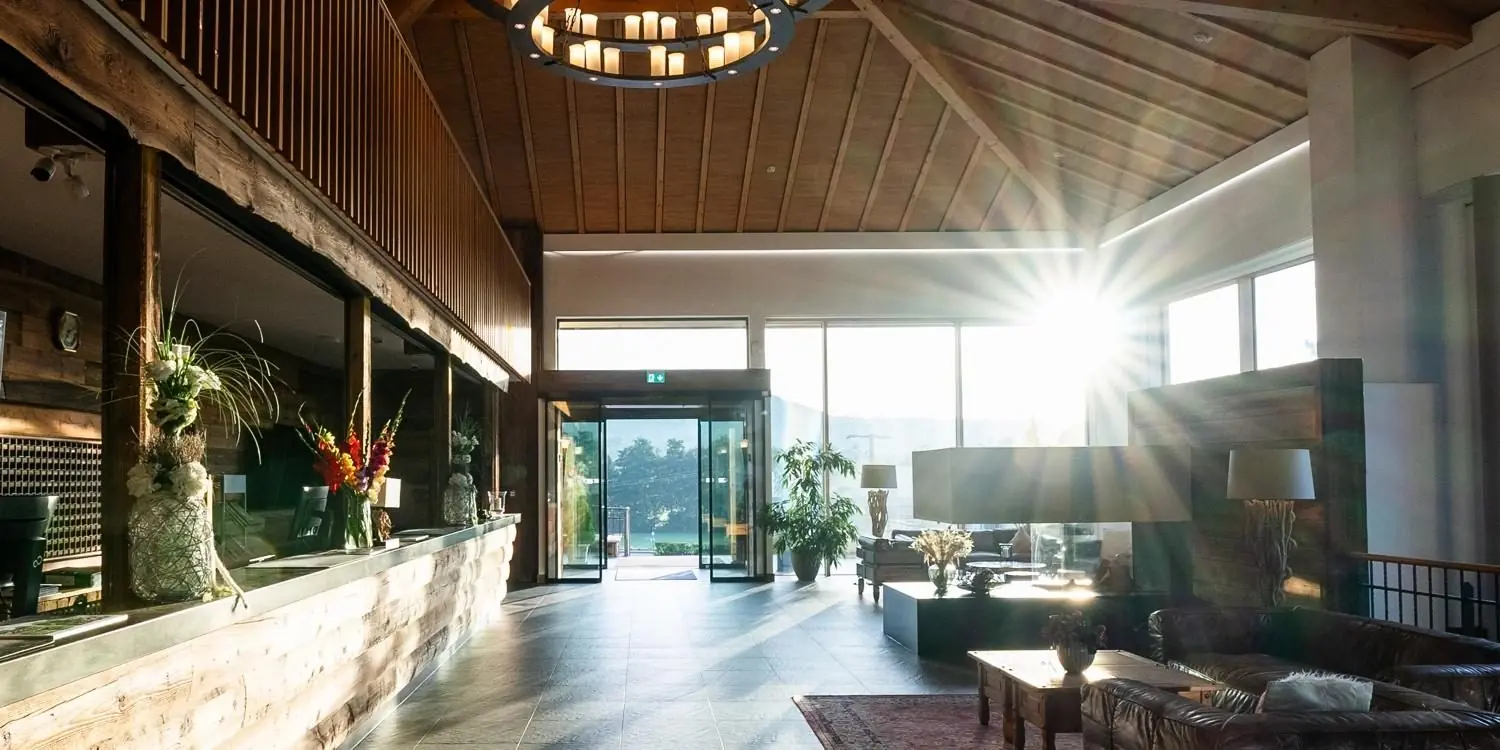 A sunlit lobby with a timber ceiling, candle chandelier and open glass doors.